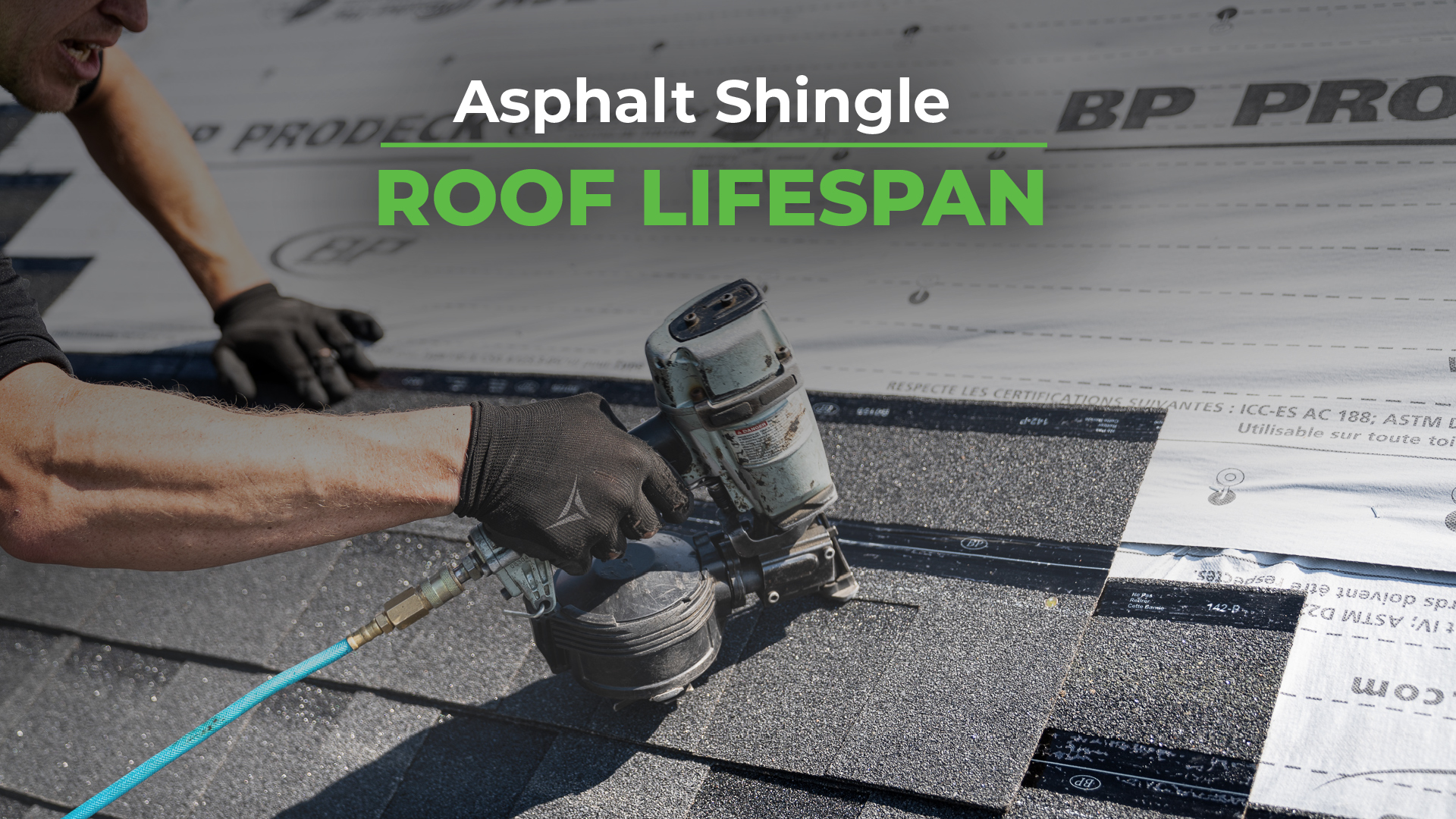 A worker wearing black gloves is using a pneumatic nail gun to install asphalt shingles on a roof, with a roofing underlayment labeled "BP ProDeck" visible in the background.