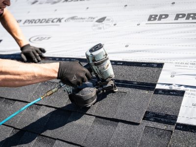 Close-up of a roofer using a nail gun to secure roofing shingles in place.