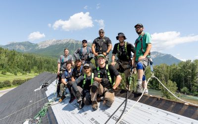 Group of roofers posing on top of a roof with harnesses, set against a Kootenay/Cranbrook mountain landscape.