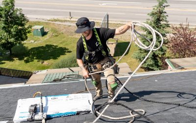 Roofer handling safety ropes and equipment on a roof with shingles and tools in the foreground.