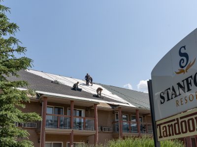 Several roofers on top of a building at Stanford Resort, installing roofing materials under a clear sky