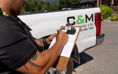 Roofer taking notes on a clipboard beside a C&M Roofing Ltd truck.